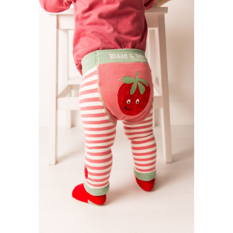 Toddler standing on a white stool wearing pink and white striped leggings with a red strawberry applique on the back pocket and red shoes. The waistband shows the brand name 'Blade & Co'.