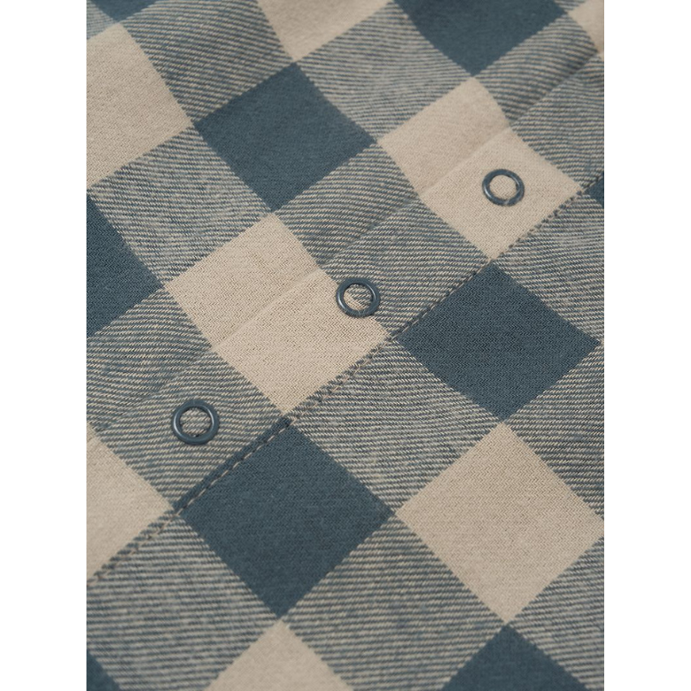 Close-up of a plaid fabric with dark blue-gray and beige squares, showing a pocket with metal snap buttons.