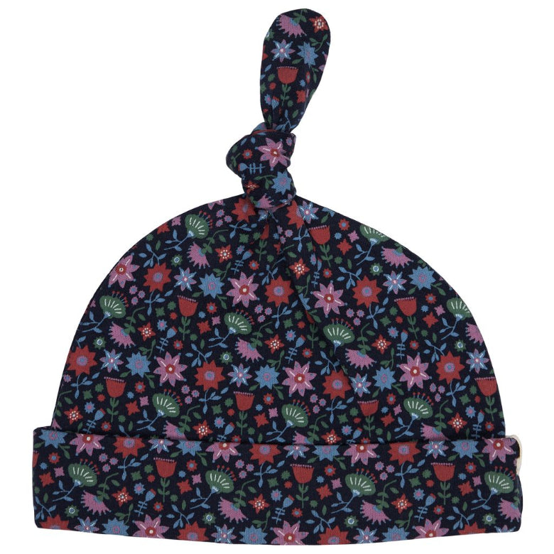 A baby knit hat with a knotted top and folded cuff, featuring a dense floral pattern in pink, blue, red, and green on a dark navy background, shown against a plain white background.