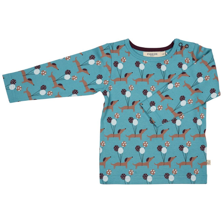 A long-sleeve baby t-shirt in a teal blue color, featuring an all-over pattern of brown dachshunds, white dandelions, and small red flowers. The brand name 'puplion' is visible on the inner neck label.