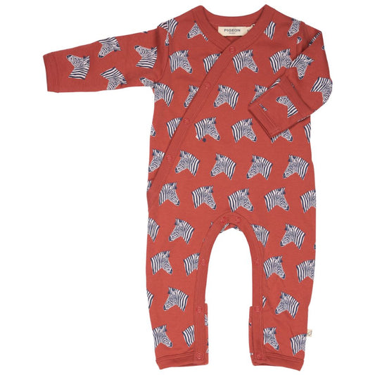 A baby long-sleeve footless one-piece romper in terracotta red, featuring an all-over print of black and white zebra heads. The romper has a snap-button closure down the front and is photographed flat against a solid white background.