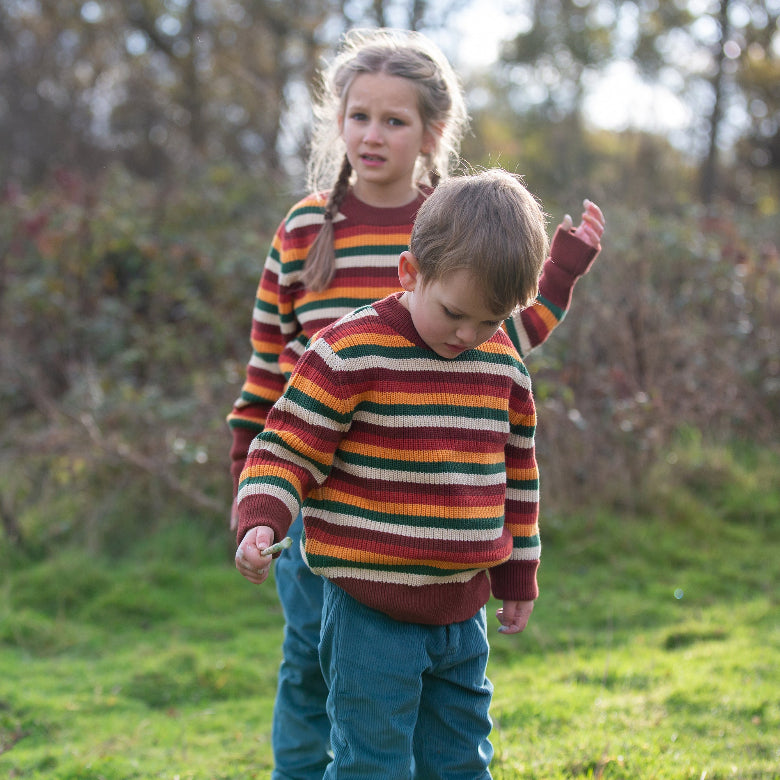 Two children wearing colorful striped sweaters walking outdoors in a natural setting.