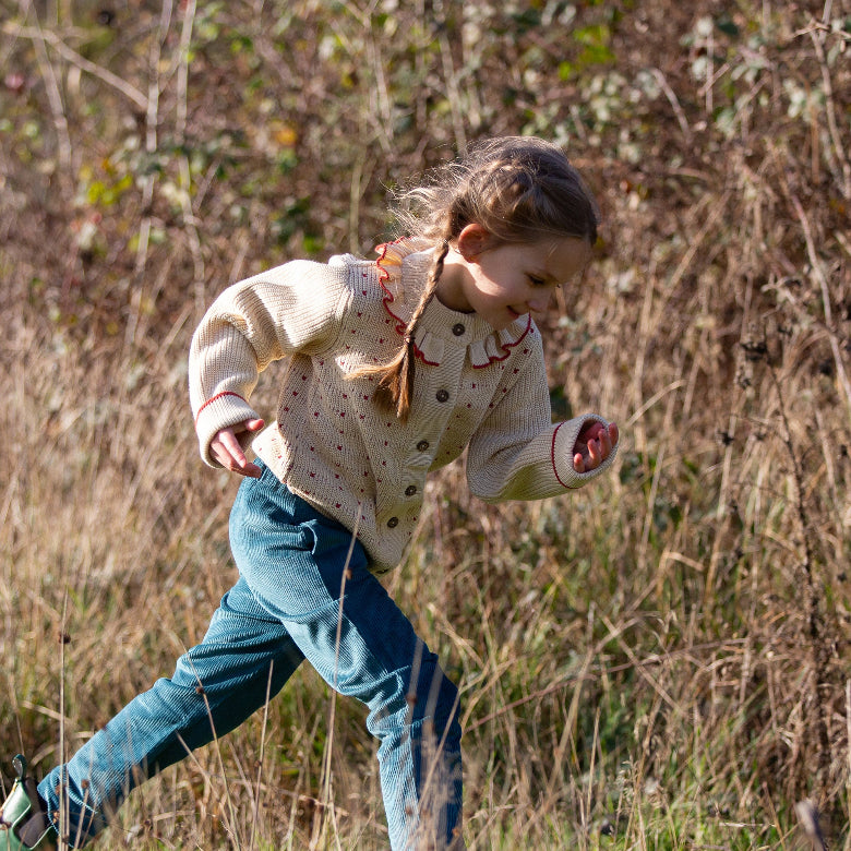 Child running through a field wearing a patterned jacket and jeans.