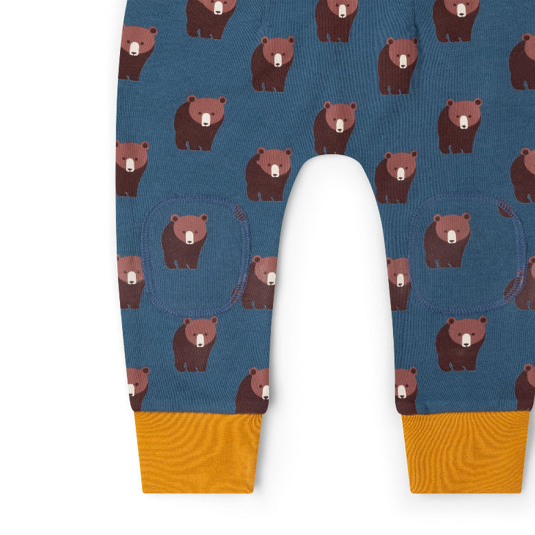 Close-up of a pair of children's leggings or pants with an allover brown bear print on a slate blue background and mustard yellow ribbed cuffs.