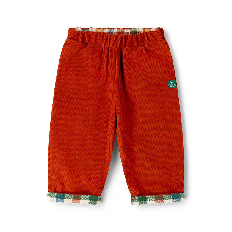 A pair of toddler corduroy pants in a rust-orange color, featuring a green brand label on the left thigh and a plaid lining visible at the elastic waistband and turned-up cuffs.