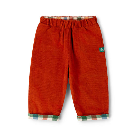 A pair of toddler corduroy pants in a rust-orange color, featuring a green brand label on the left thigh and a plaid lining visible at the elastic waistband and turned-up cuffs.