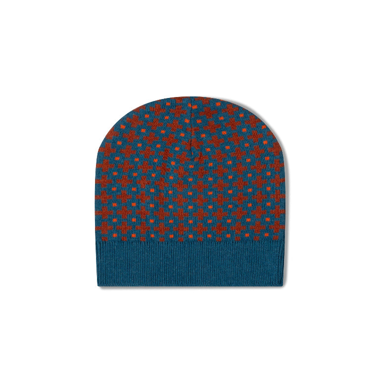A knit beanie hat with a geometric pattern of red and blue stars and dots on a dark teal background, featuring a solid ribbed cuff at the bottom.