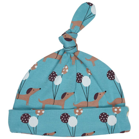 A baby knit hat in a light teal blue color, featuring a playful pattern of dachshunds and balloons. The hat has a knotted top and a folded cuff, shown against a plain white background.