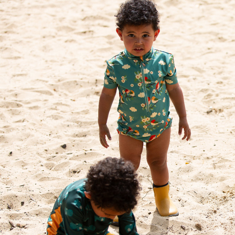 Two children in matching swimsuits and rain boots on a sandy beach.