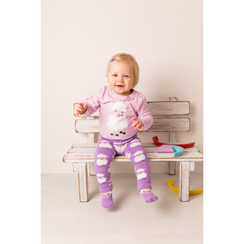A baby sitting on a rustic wooden bench wearing a light pink long-sleeve pajama top with a white sheep graphic and matching purple patterned pajama pants with white sheep prints.