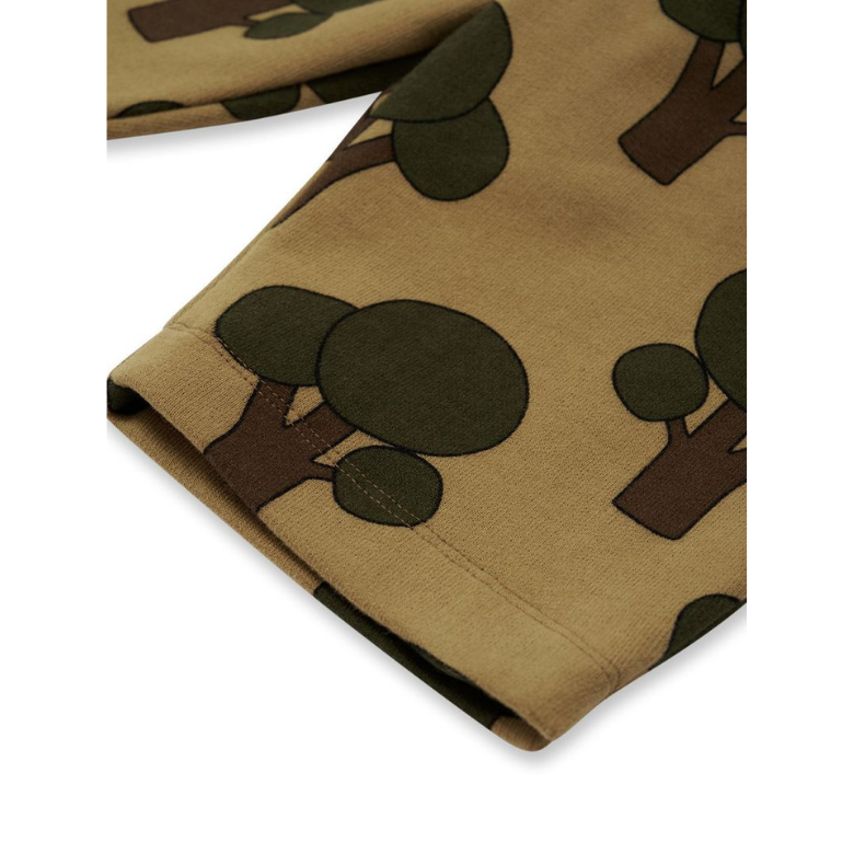 A close-up of a garment sleeve or folded fabric showing a tan base with a dark olive green and brown tree print, photographed on a white background.