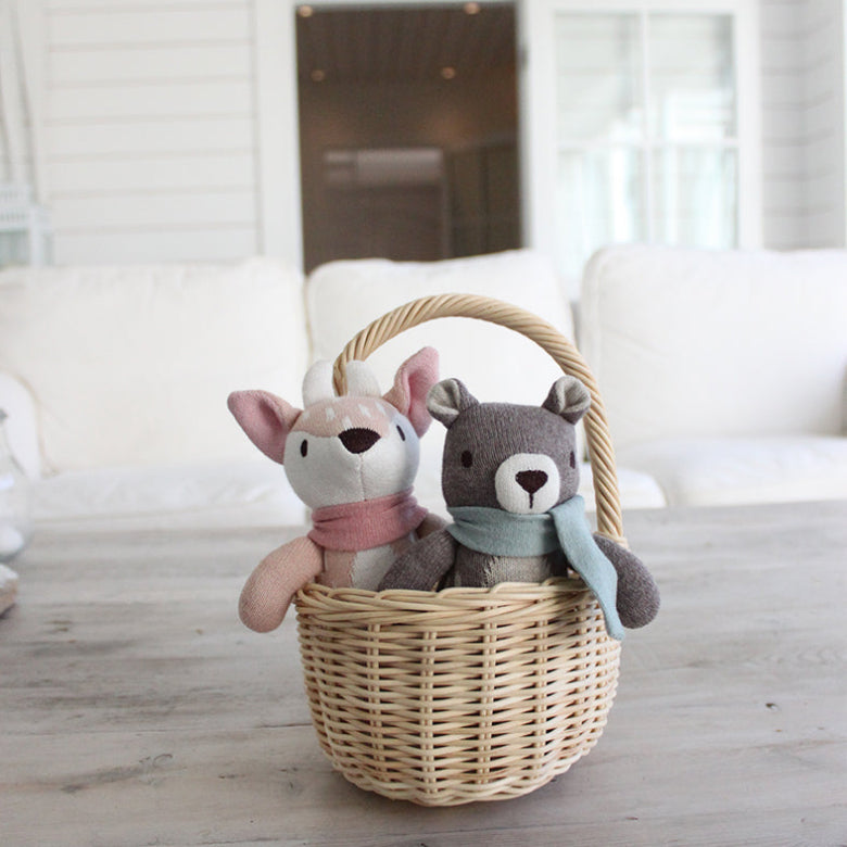Two stuffed animal toys in a wicker basket on a wooden floor with a blurred indoor background.