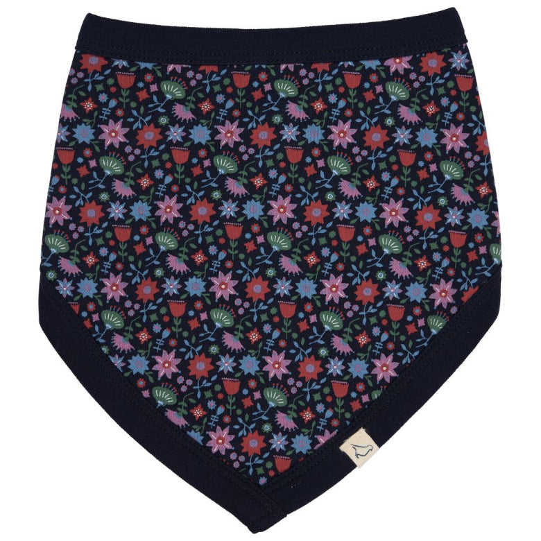 A baby bandana bib with a dark navy blue background and an all-over colorful floral and leaf pattern in pink, blue, green, and red. It features solid navy blue trim along the edges and a small white brand tag near the bottom right corner.