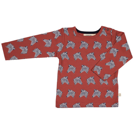 A long-sleeve children's top in terracotta red, featuring an all-over print of black and white zebra heads. The shirt is laid flat against a solid white background.