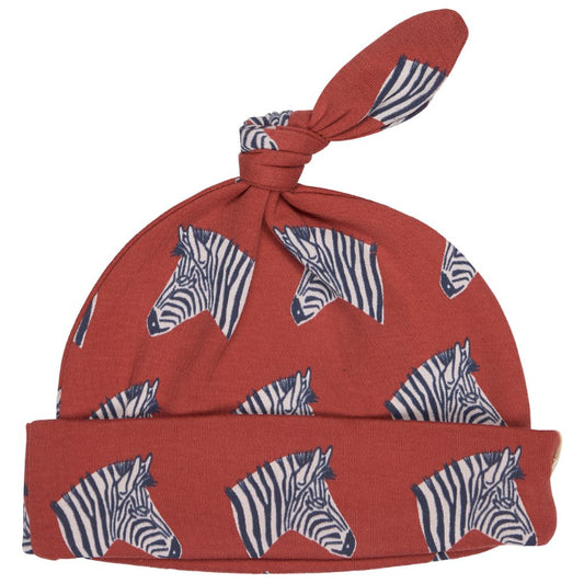 A terracotta red baby hat with a knotted top and a folded cuff, both printed with a navy and white zebra pattern, shown on a plain white background.