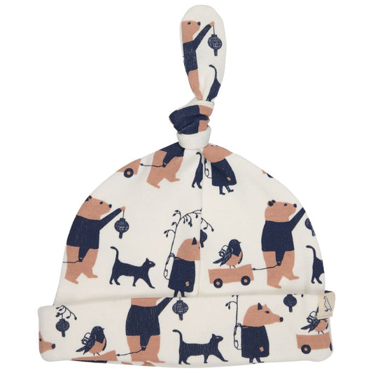 A baby knit hat with a knotted top and folded cuff, featuring an all-over print of teddy bears, dogs, and birds in navy blue and tan on an off-white background.