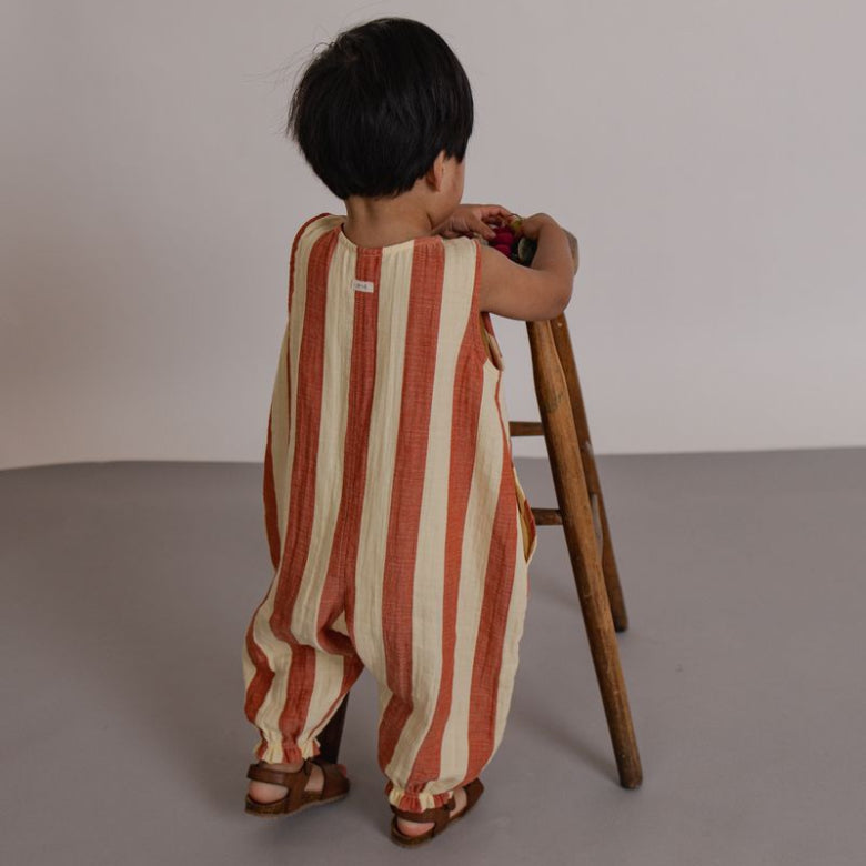 Child wearing a striped romper standing on a stool against a plain background