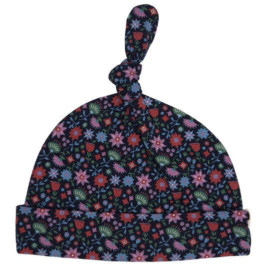 A baby knit hat with a knotted top and folded cuff, featuring a dense floral pattern in pink, blue, red, and green on a dark navy background, shown against a plain white background.